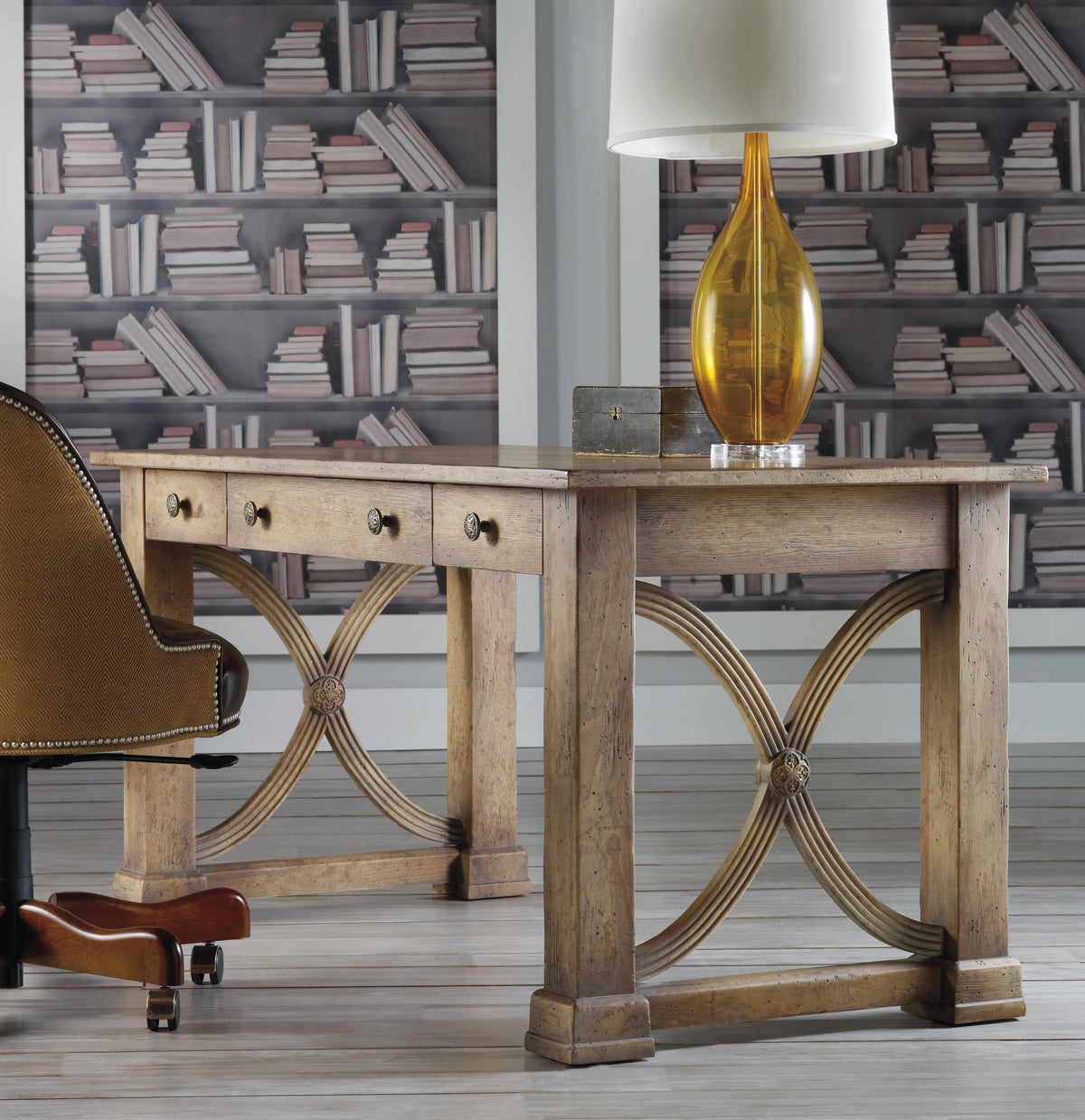a desk with a lamp and a chair in front of a wallpaper