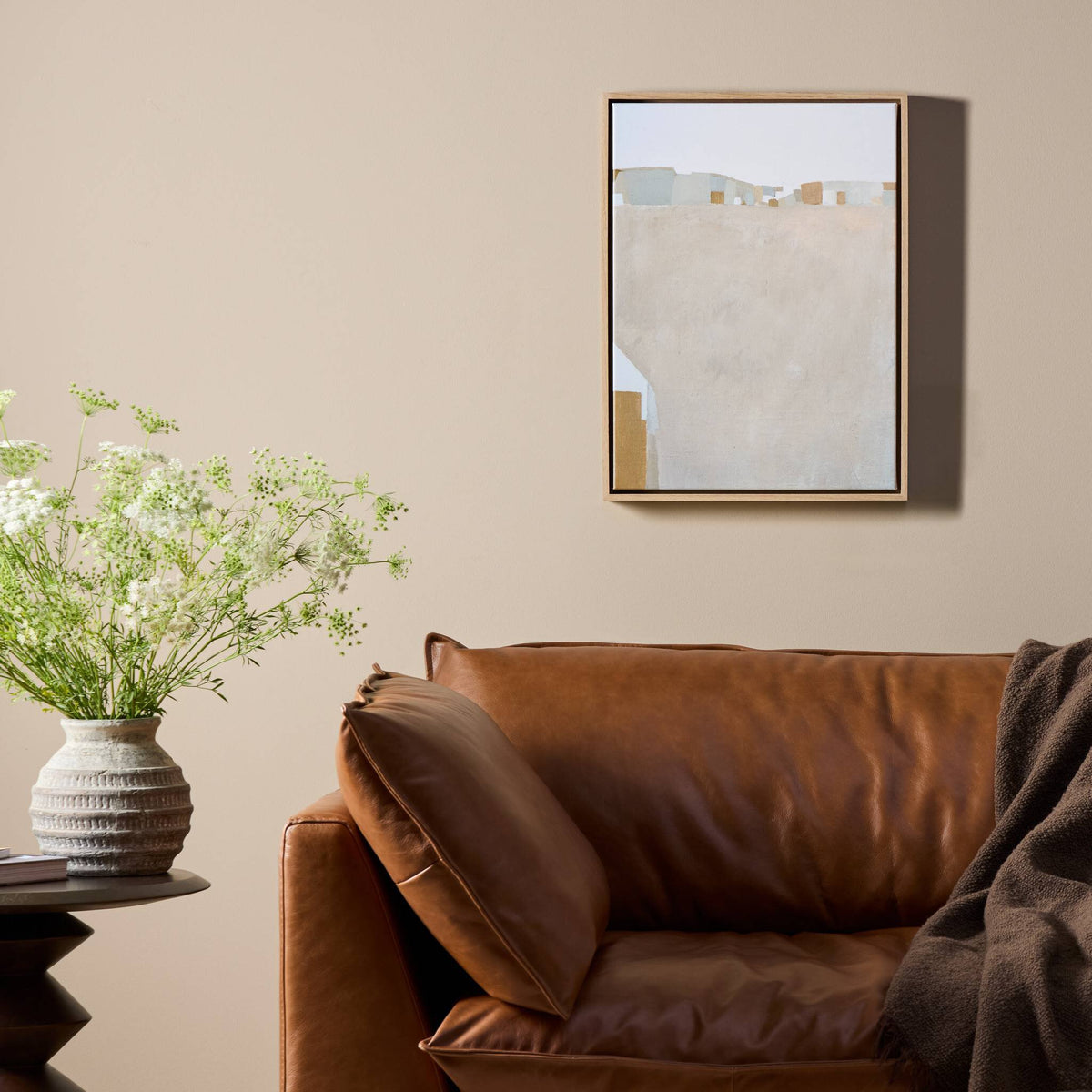 a brown couch with a brown blanket and a vase of flowers on a table