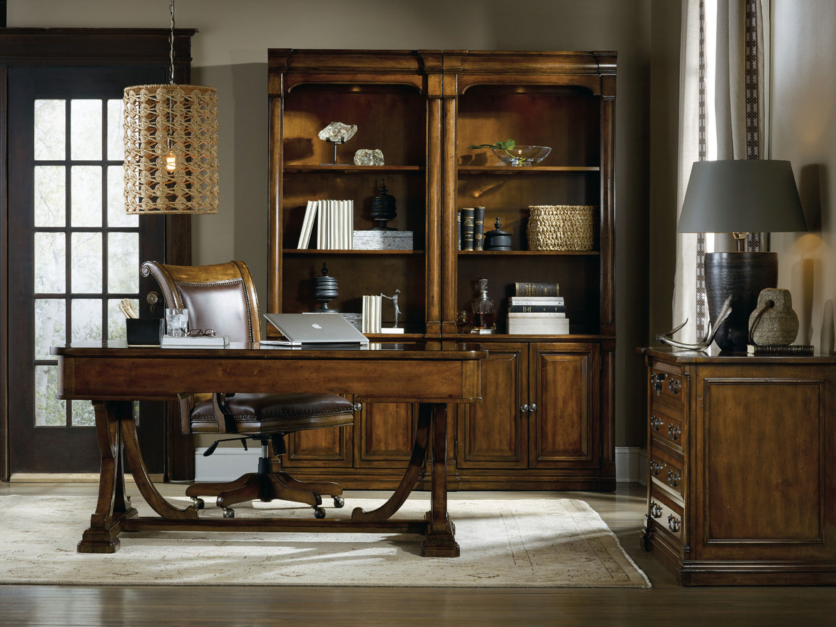 a desk in a room with a bookcase and lamp