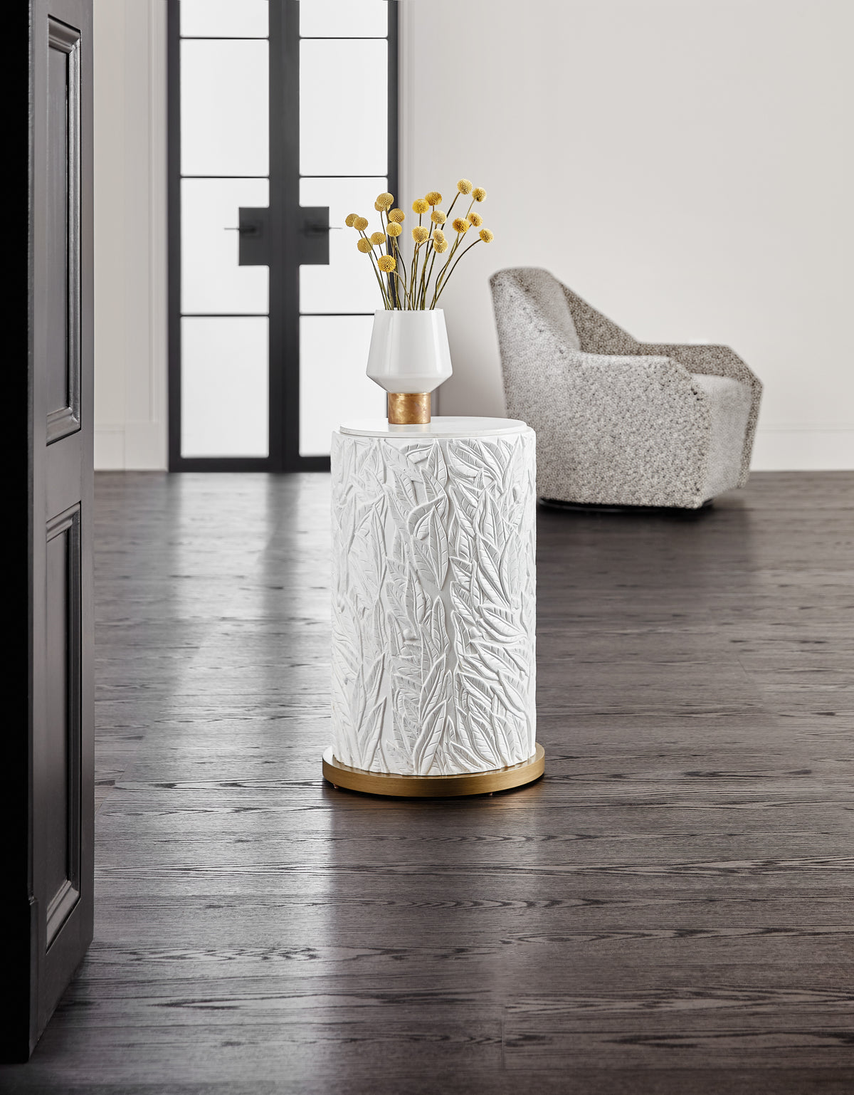 a white vase with yellow flowers on a pedestal in a room